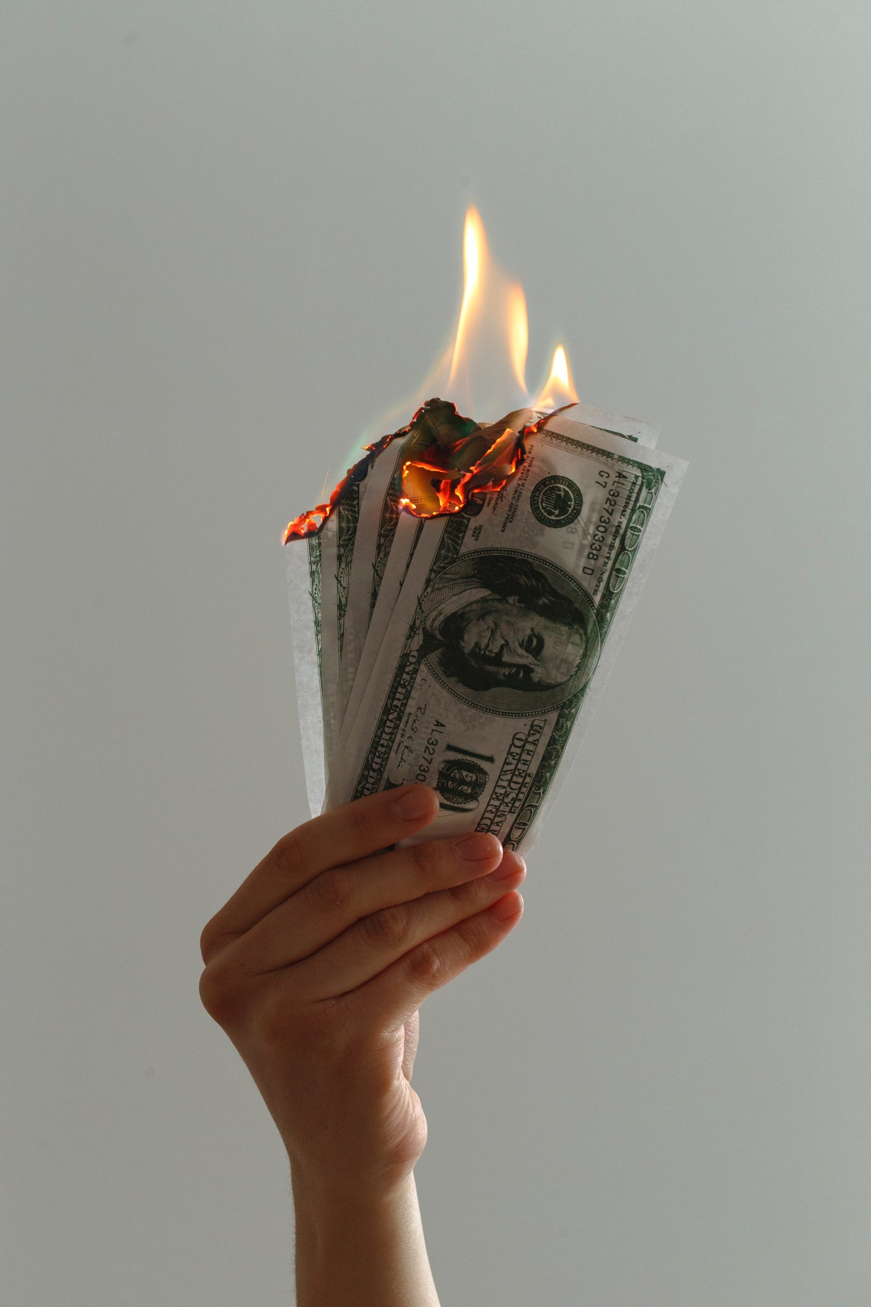 hand holding 4 hundred dollar bills that are on fire