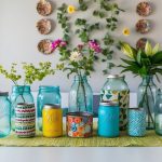 A table with repurposed glass jars, cans, and fabric, transformed into vases, organizers, and wall art. Plants and flowers add a touch of nature